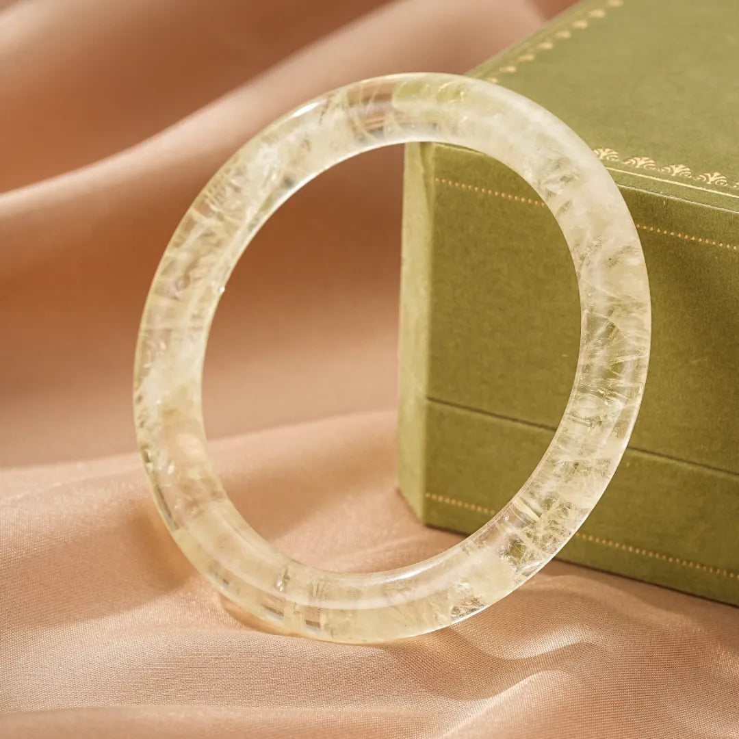 Bracelet jonc en citrine naturelle aux reflets lumineux, monté sur un fond de soie beige et à côté d'une boîte verte.