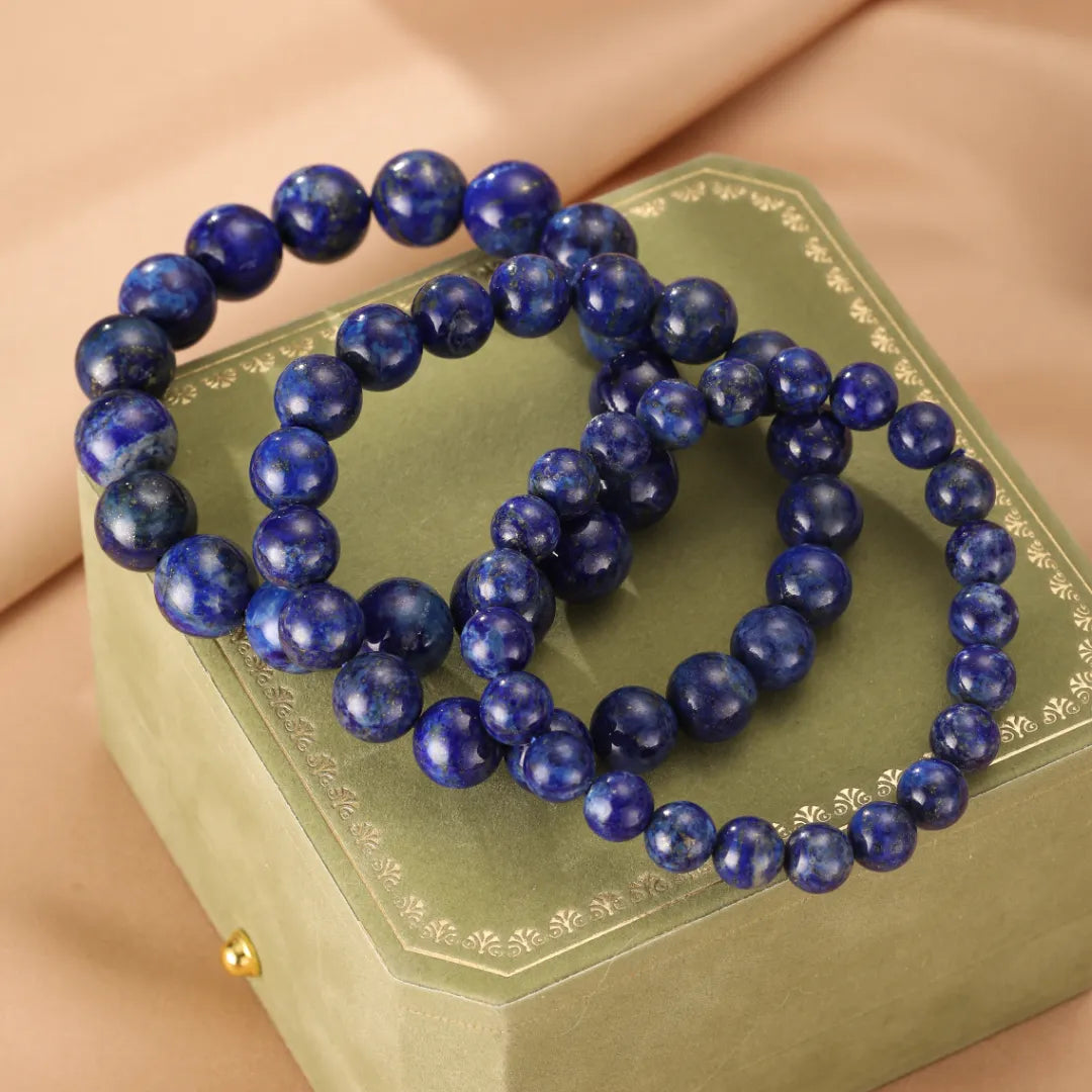 Deux bracelets de perles rondes en lapis-lazuli bleu profond disposés sur une boîte verte.
