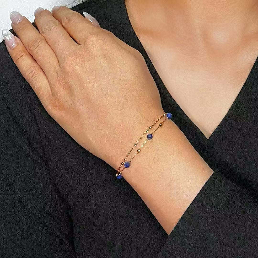 Bracelet double chaîne or rose avec perles bleues de lapis-lazuli porté au poignet d'une femme.