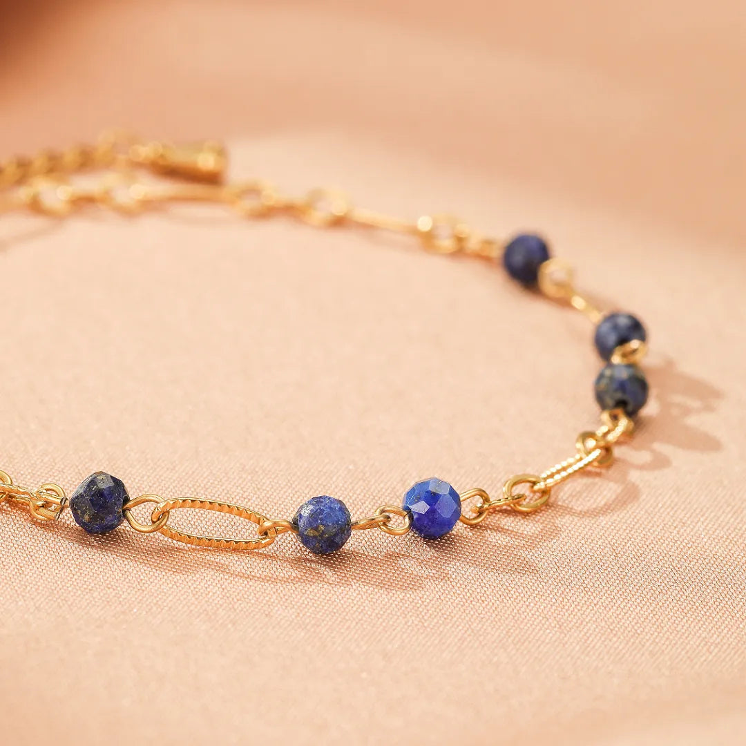 Bracelet fin en plaqué or avec des perles rondes et facettées de lapis-lazuli bleu profond et un élément central ovale texturé.