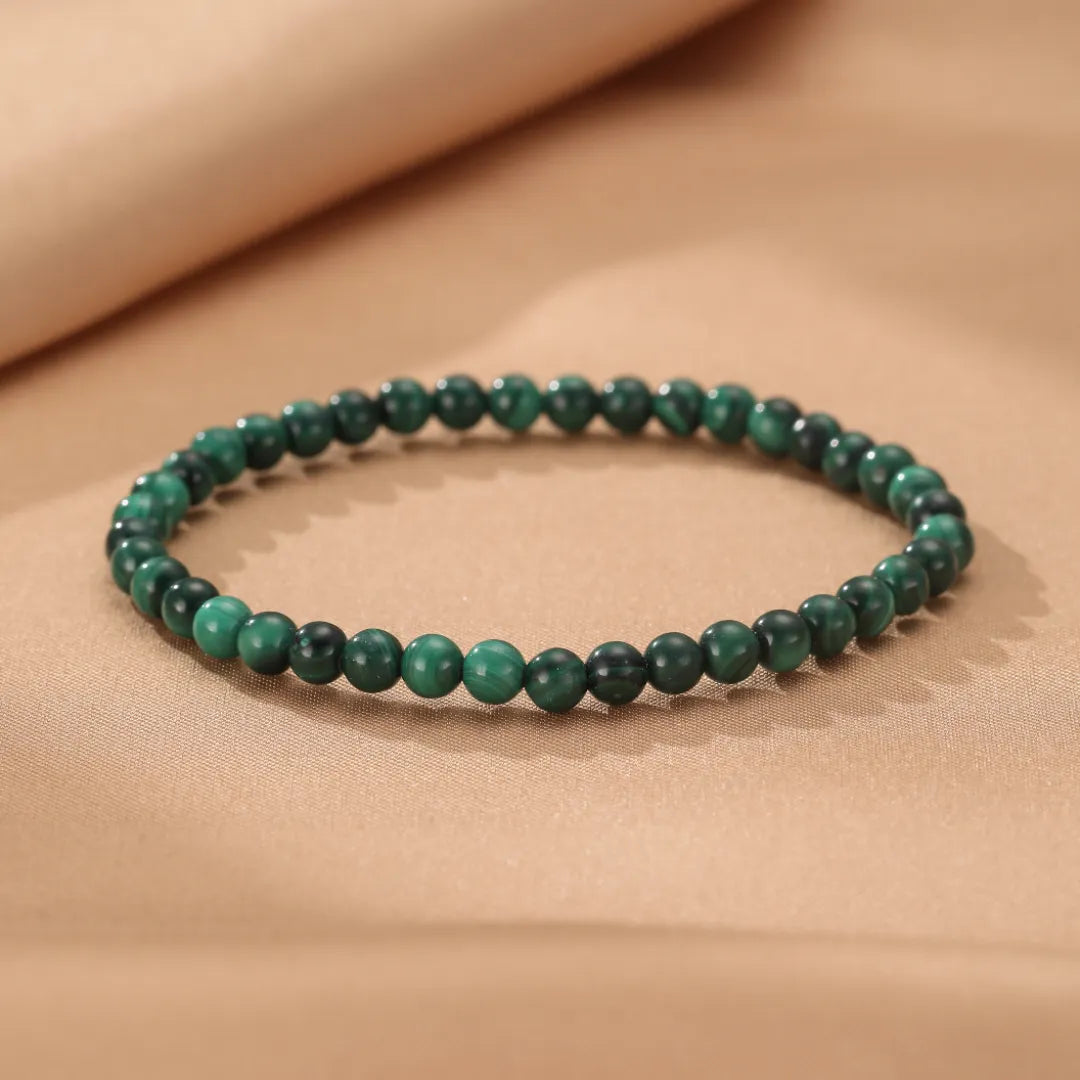 Bracelet Malachite "Veines Vertes" composé de perles rondes d'un vert profond avec des marbrures caractéristiques de la malachite, posé sur un fond beige satiné.