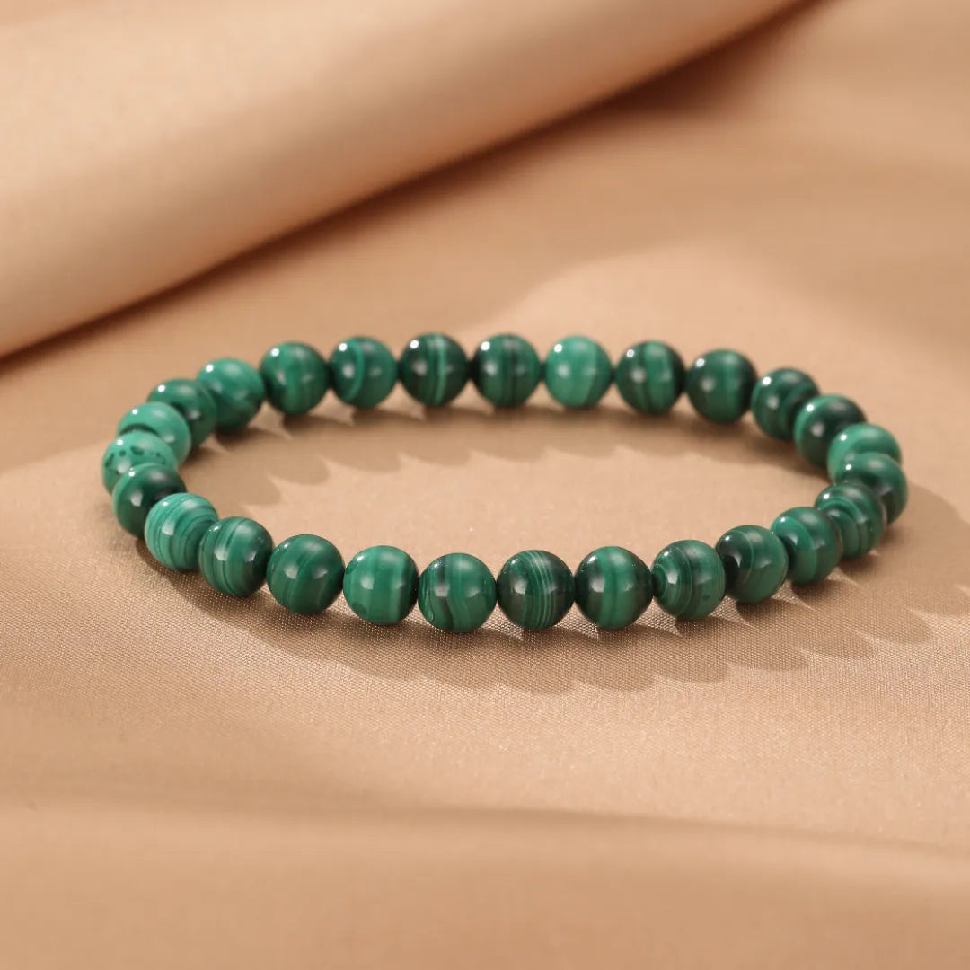 Bracelet en perles de malachite naturelle aux veines vertes distinctives, posé sur un fond beige satiné.