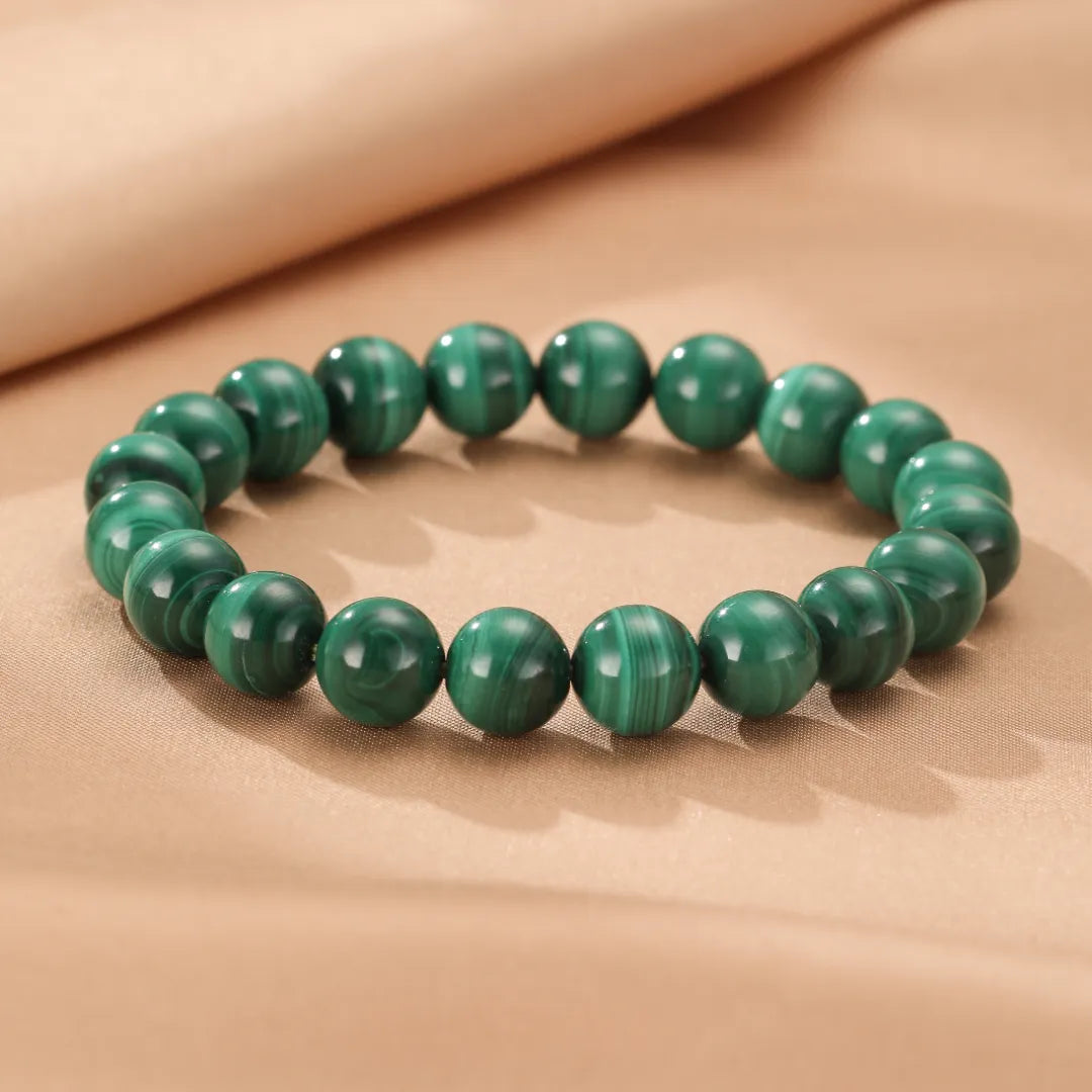 Bracelet de perles rondes en malachite naturelle aux veines vertes distinctives, posé sur un fond beige texturé.