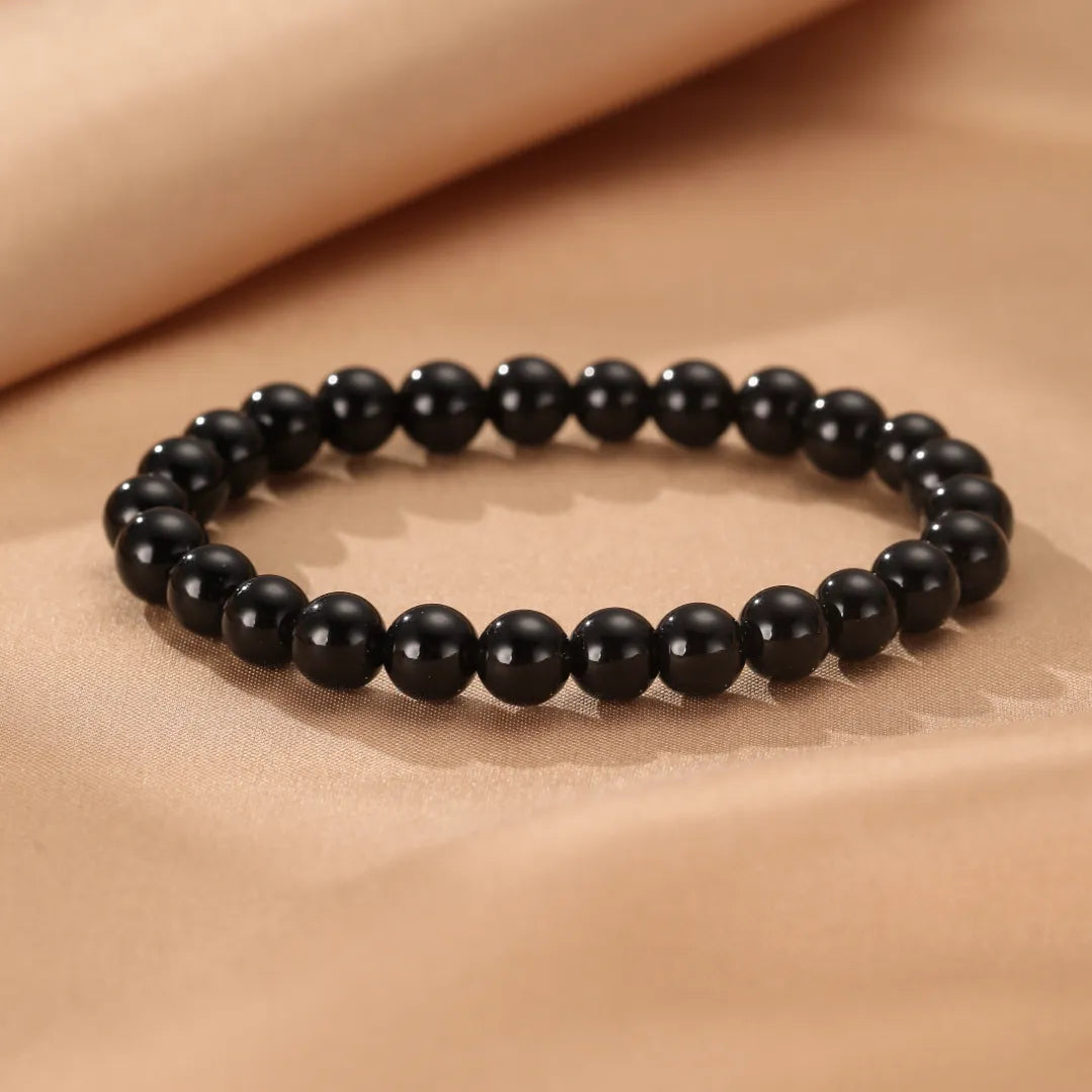 Bracelet fait de perles d'obsidienne noire polie, posé sur un fond texturé de couleur beige.