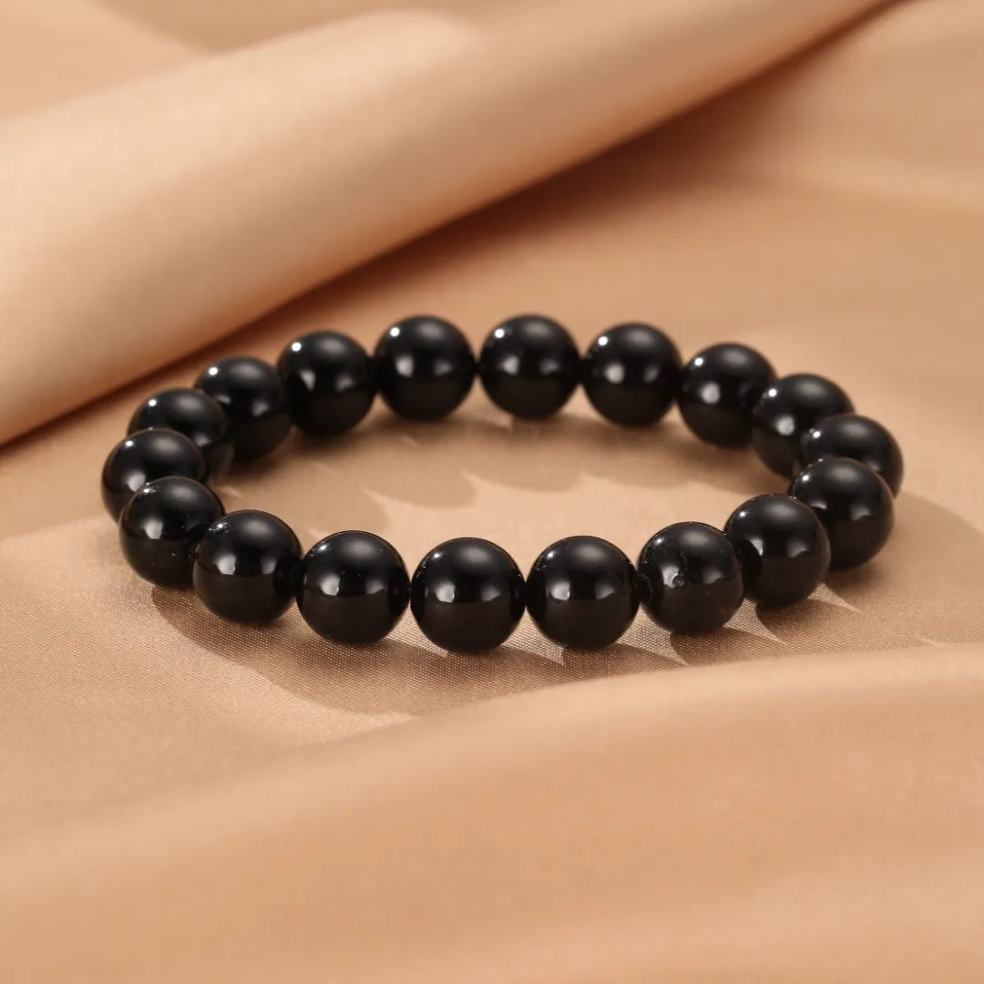 Bracelet fait de perles rondes d'obsidienne noire, posé sur un tissu beige satiné.