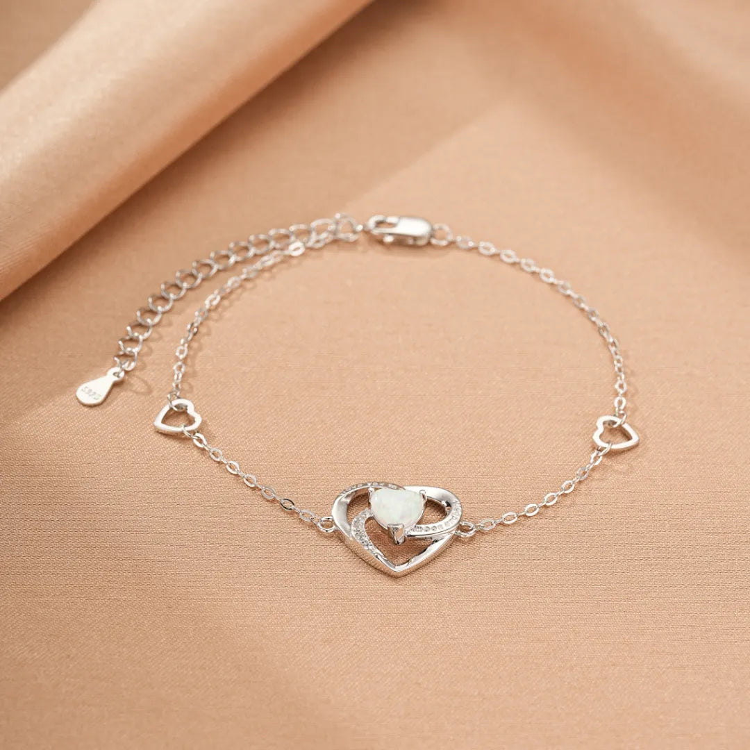 Bracelet en argent avec un pendentif en forme de cœur double, incrusté d'une opale blanche et entouré de petits cœurs creux.