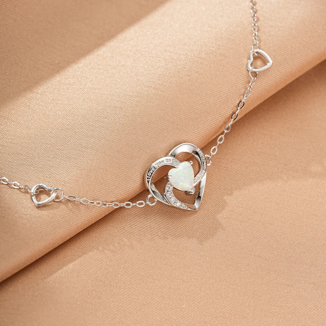 Bracelet en argent 925 avec un cœur central en opale blanche entouré de petits cœurs et de zircons cubiques. Le bracelet est orné de plusieurs petits cœurs ajourés le long de la chaîne.