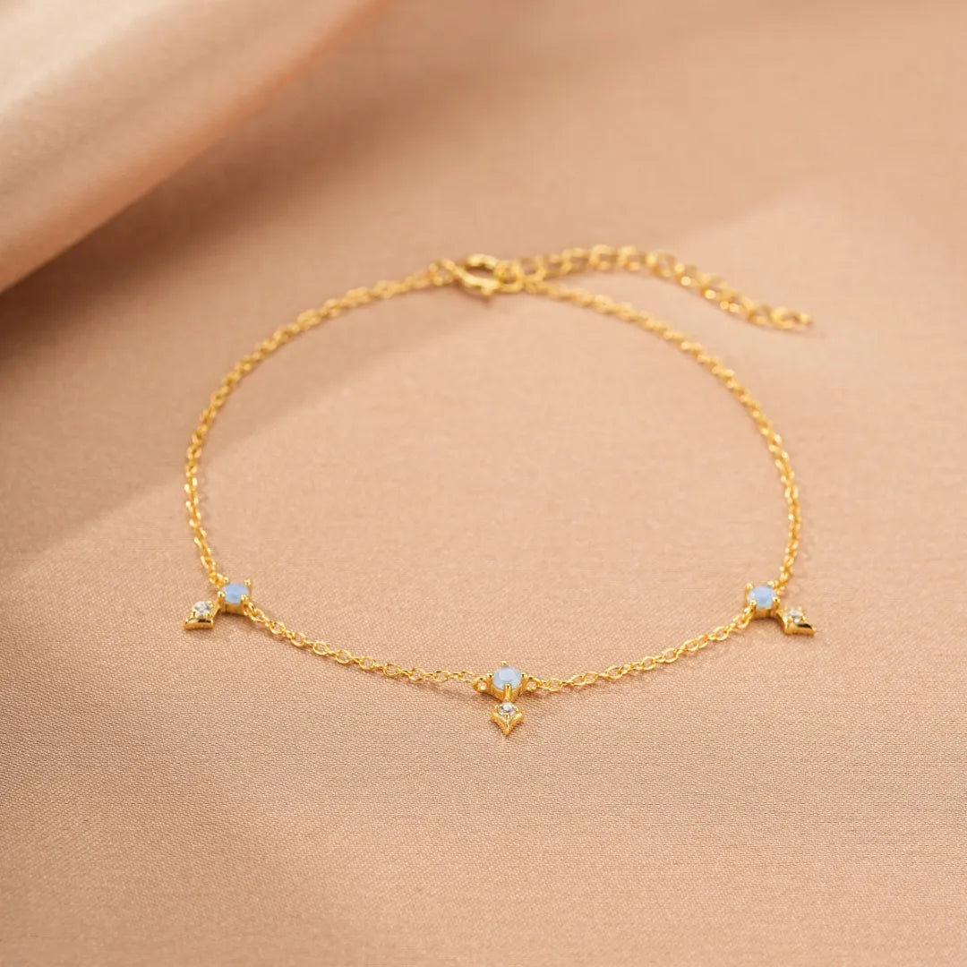 Bracelet fin en argent doré or avec trois ornements en forme de croix sertis de petites opales et de zircons cubiques, sur fond beige satiné sur fond beige.
