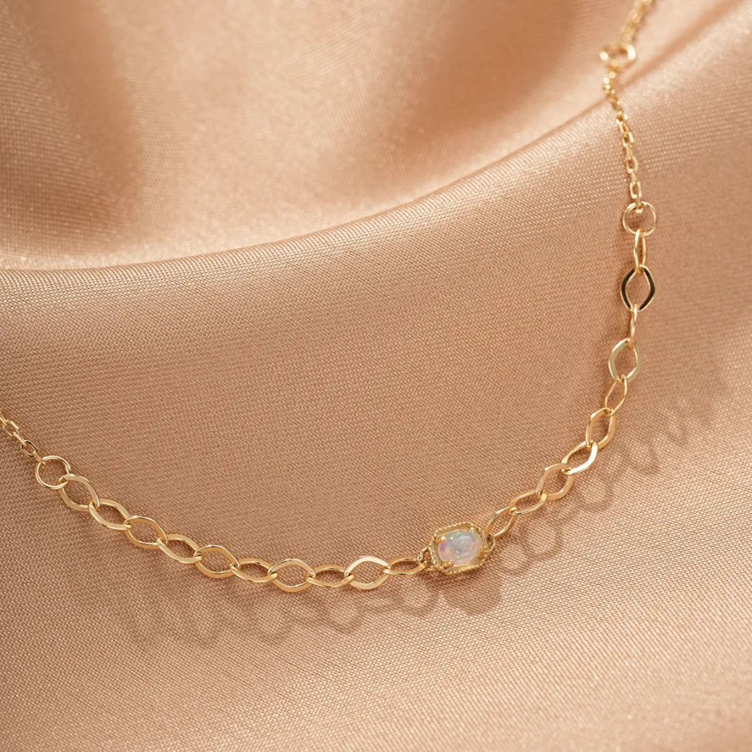 Bracelet en argent doré à l'or avec une petite opale rectangulaire au centre, sur fond satiné couleur champagne.