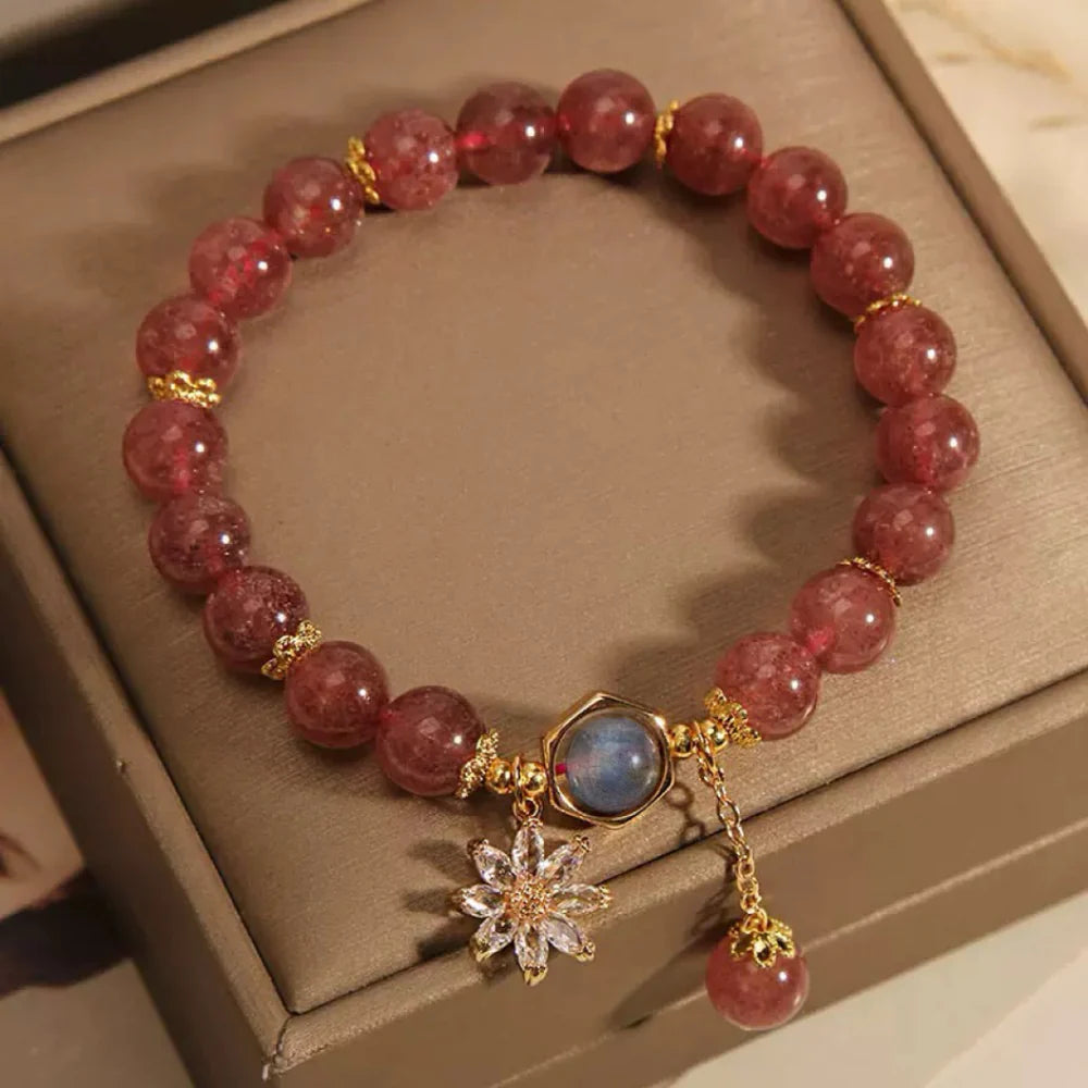 Bracelet avec des perles roses de quartz fraise et un pendentif fleur en cristal de roche, rehaussé d'une pierre bleue hexagonale et d'une breloque en quartz fraise.