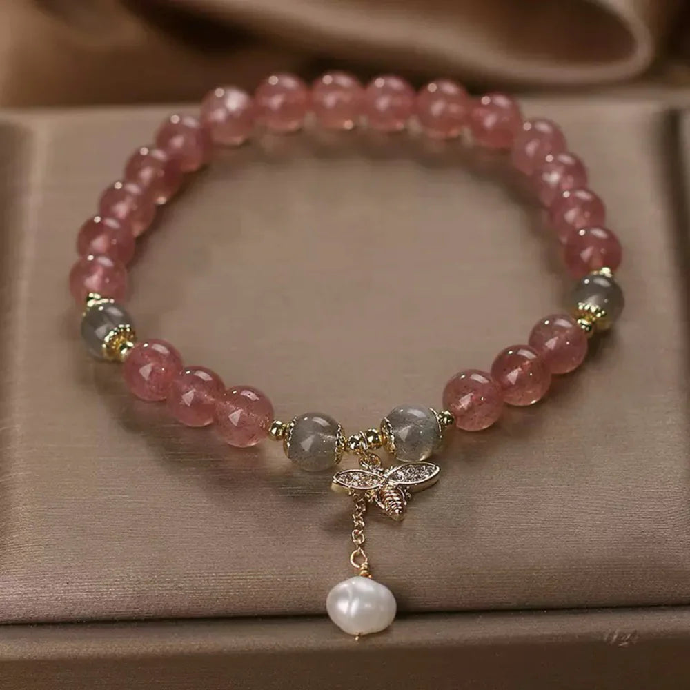 Bracelet élastique fait de perles de quartz fraise roses, de perles de labradorite grises et d'un pendentif abeille orné de zirconiums, agrémenté d'une perle d'eau douce blanche suspendue.