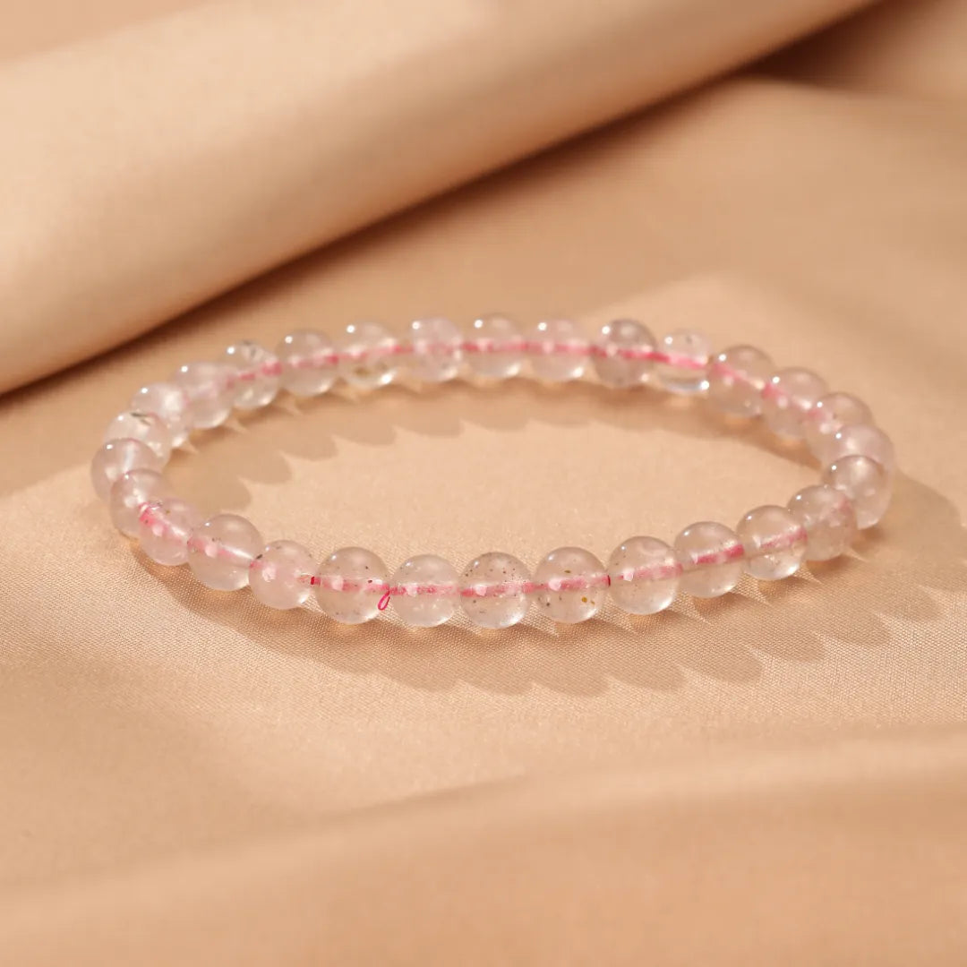 Bracelet en quartz fraise "Rose Doux" avec de petites perles roses et scintillantes, présenté sur un fond de tissu satiné beige.