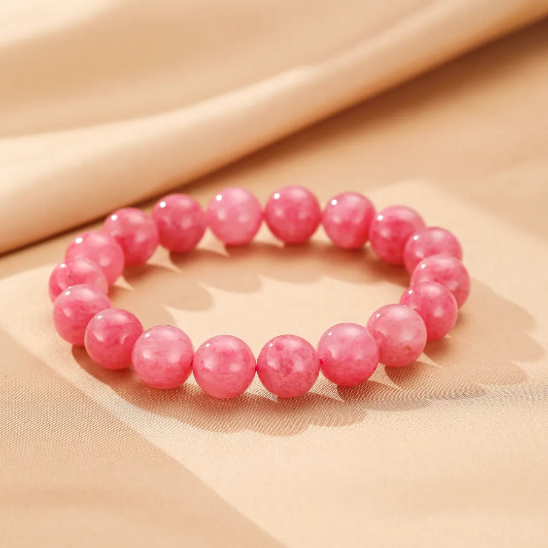 Bracelet "Rose Tendre" en rhodonite avec des perles rondes rose vif, présenté sur un fond texturé beige.