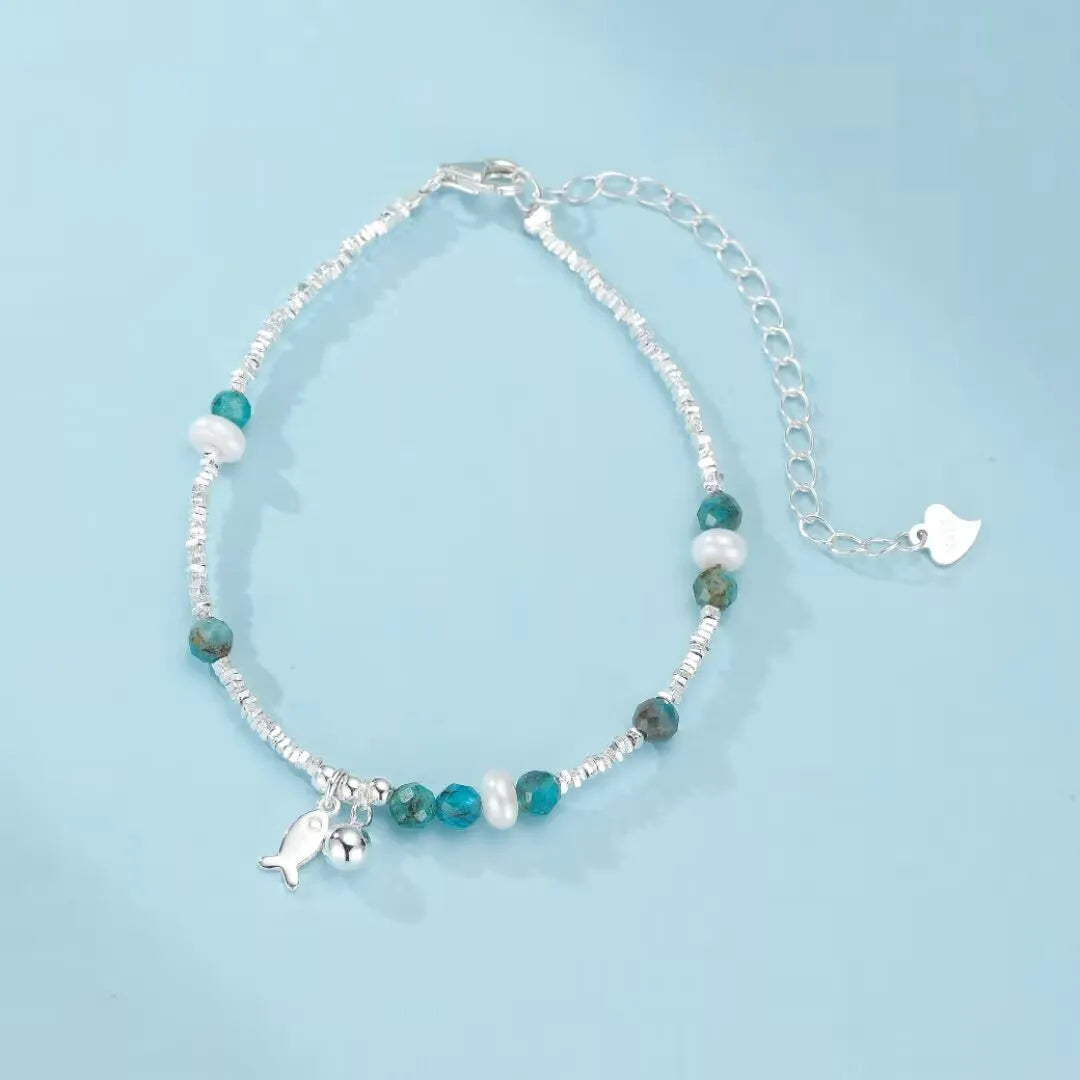 Bracelet en argent 925 avec des perles d'apatite bleue, des perles d'eau douce blanches, un pendentif poisson et une breloque clochette.