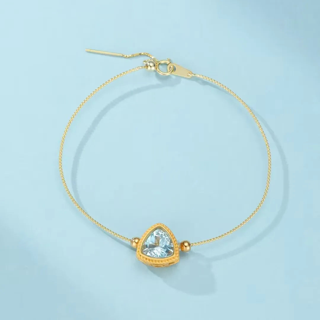 Bracelet fin en argent doré orné d'une topaze bleue triangulaire centrale et de deux petites perles dorées, fermoir ajustable.