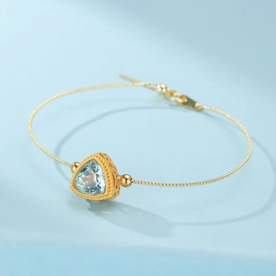 Bracelet fin en argent doré serti d'une topaze bleue en forme de triangle, orné de petites billes dorées.