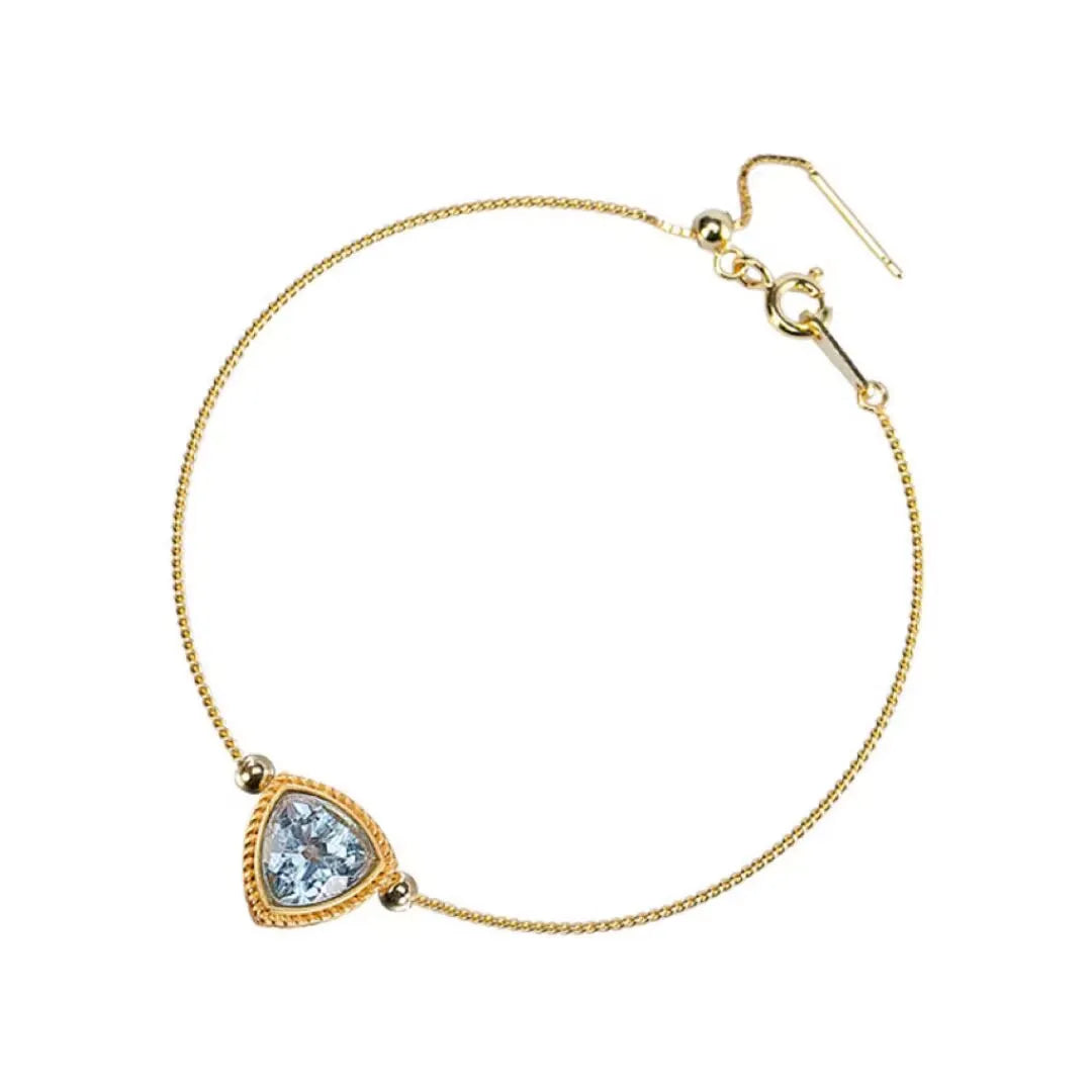 Bracelet fin en argent doré or avec une topaze bleue taillée en triangle, sertie dans un entourage texturé et ornée de deux petites billes d'argent doré or.