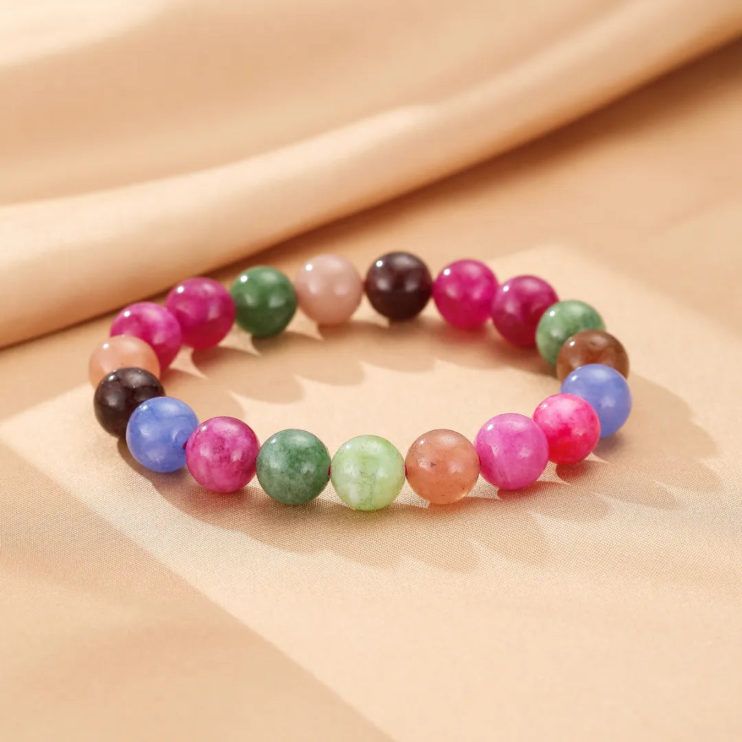 Bracelet "Équilibre Coloré" en tourmaline avec des perles multicolores rondes et polies, posé sur un fond beige doux.