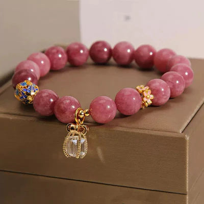 Bracelet "Raffinement Impérial" en tourmaline rose et cristal de roche, orné d'un pendentif couronne et d'un fermoir fleuri.