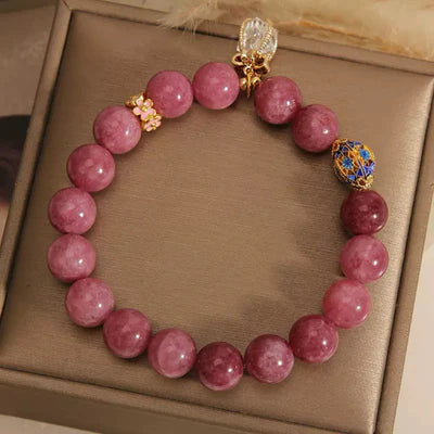 Bracelet en tourmaline rose et cristal de roche avec des breloques en forme de fleur et un élément bleu et doré.