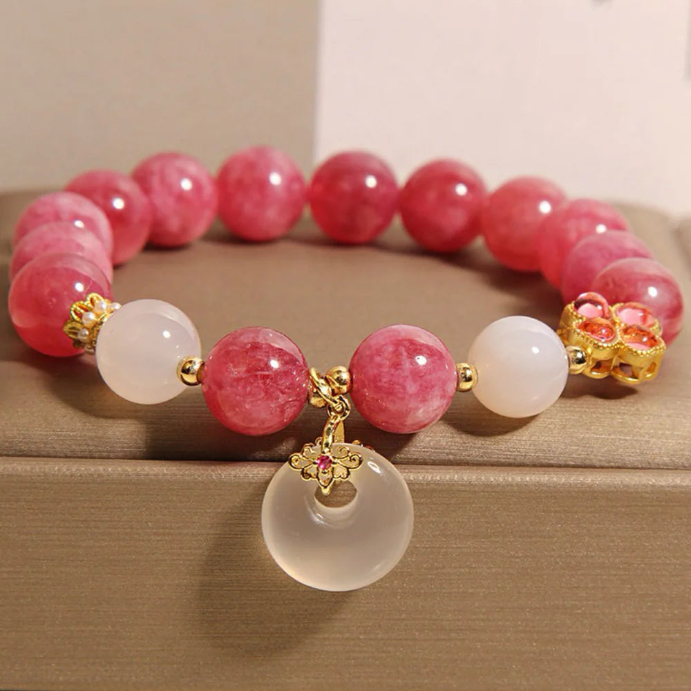 Bracelet "Douceur Éclatante" fait de perles de tourmaline rose et de jade blanc, avec un pendentif rond en jade et des détails dorés en forme de trèfle.