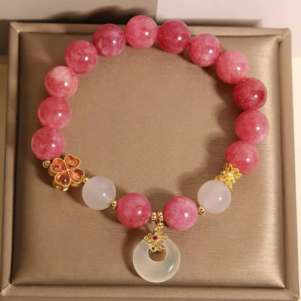 Bracelet "Douceur Éclatante" orné de perles de tourmaline rose, de jade blanc, d'un trèfle doré et d'une breloque ronde en jade blanc avec une pierre rouge au centre.