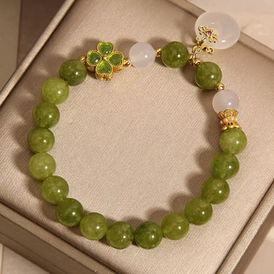 Bracelet "Rayons d'Optimisme" avec un trèfle émaillé vert, des perles de tourmaline verte et de jade, et une pierre blanche, monté sur fil élastique.