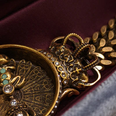 Gros plan sur un bracelet vintage doré orné de zirconiums et d'une petite grenouille incrustée de pierres turquoise et blanches, avec une couronne stylisée.
