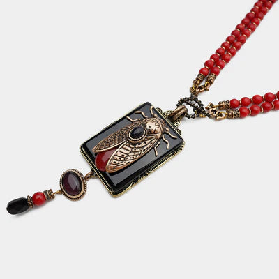 Collier fantaisie avec pendentif rectangulaire noir orné d'une cigale dorée, d'une agate rouge et d'une petite pierre noire, monté sur deux rangs de perles rouges corail.