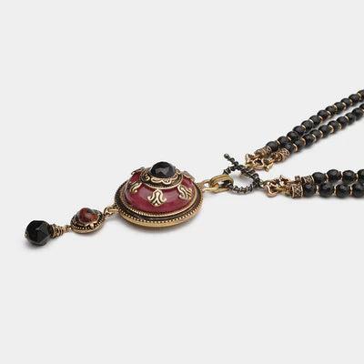 Collier Agate "Merveille d'Antan" avec pendentif rond rouge orné d'une pierre noire et de détails dorés, double rang de perles noires.