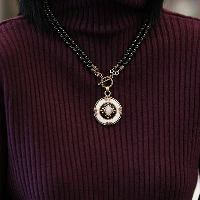 Collier Agate Noire "Pureté Mystique" avec pendentif rond blanc et détails dorés, porté sur un pull à col roulé bordeaux