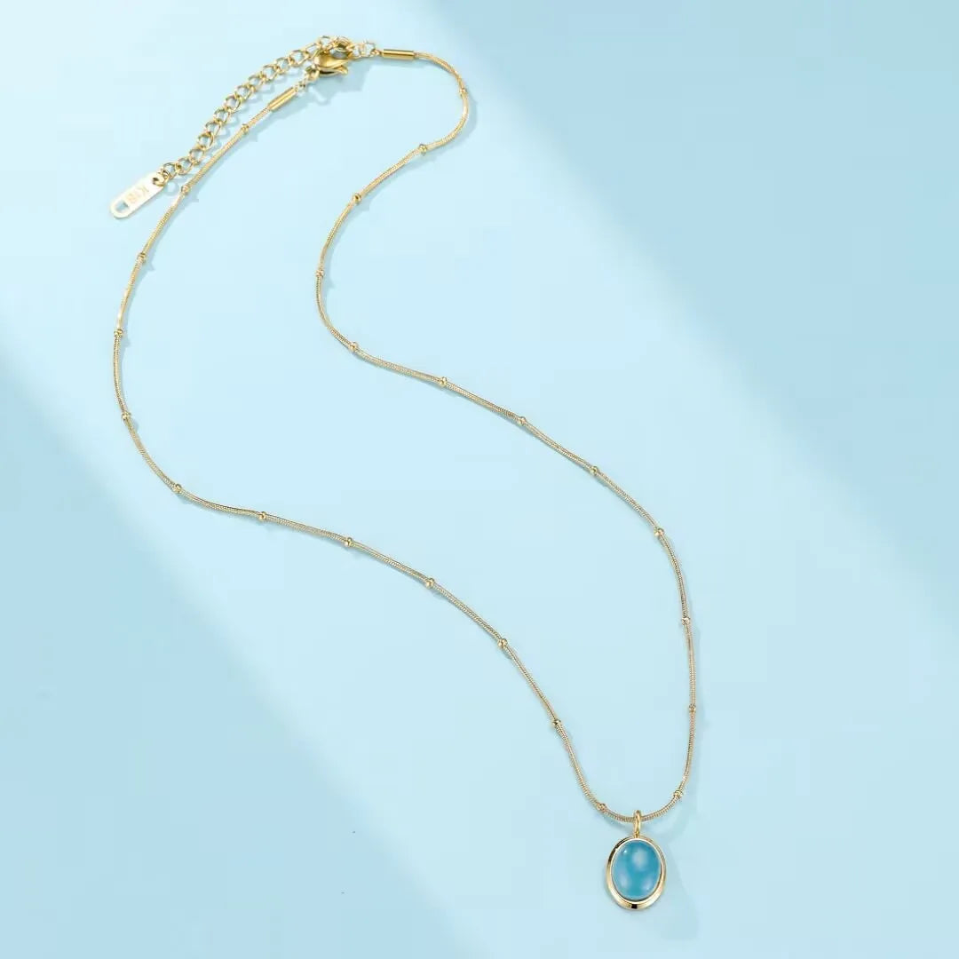 Collier "Clarté Céleste" avec pendentif ovale en aigue-marine bleue, monté sur une chaîne fine dorée à l'or 18 carats en acier titane.