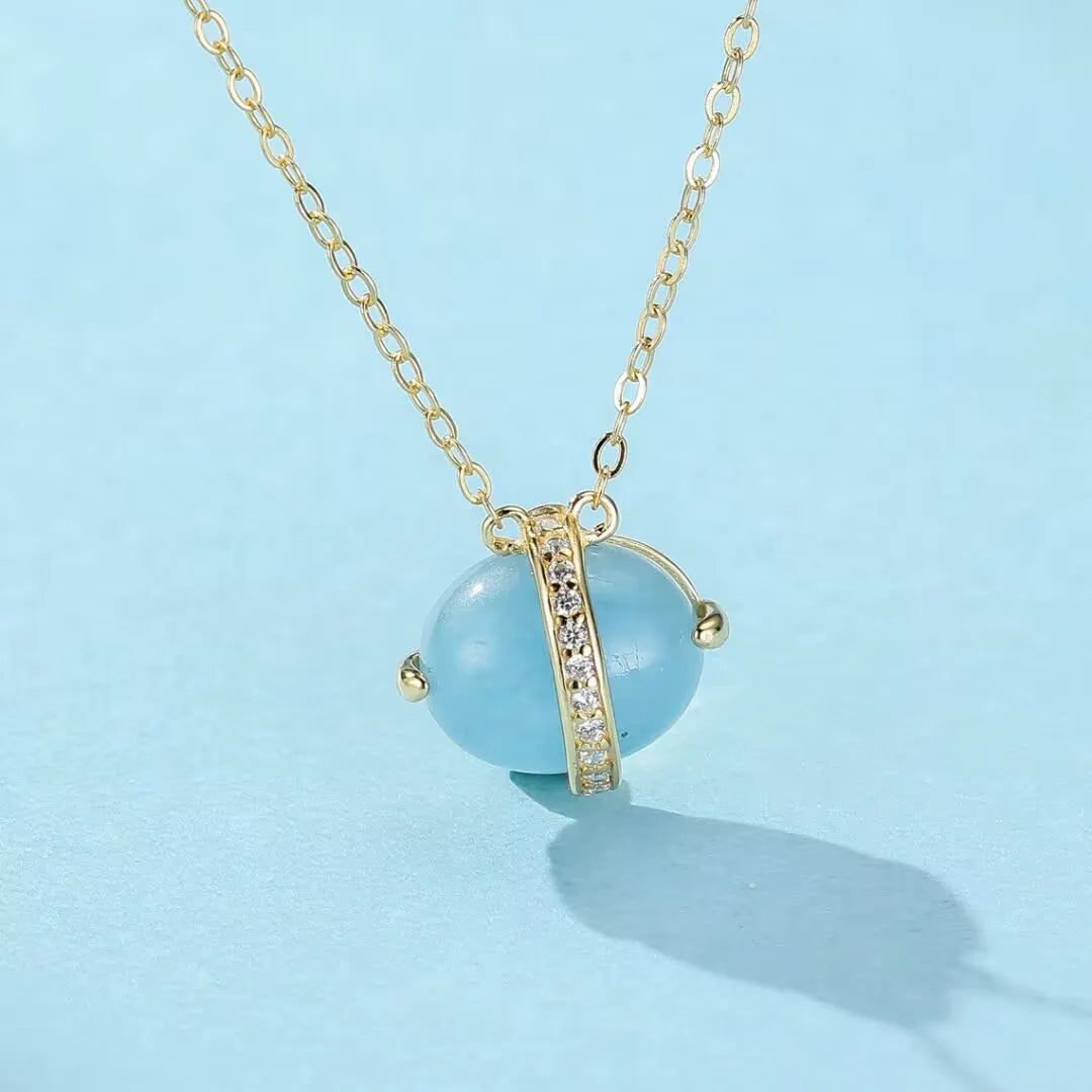 Collier "Galaxie Bleue" en argent doré or 14K avec pendentif ovale en aigue-marine bleu clair entouré d'une bande d'oxydes de zirconium brillants.