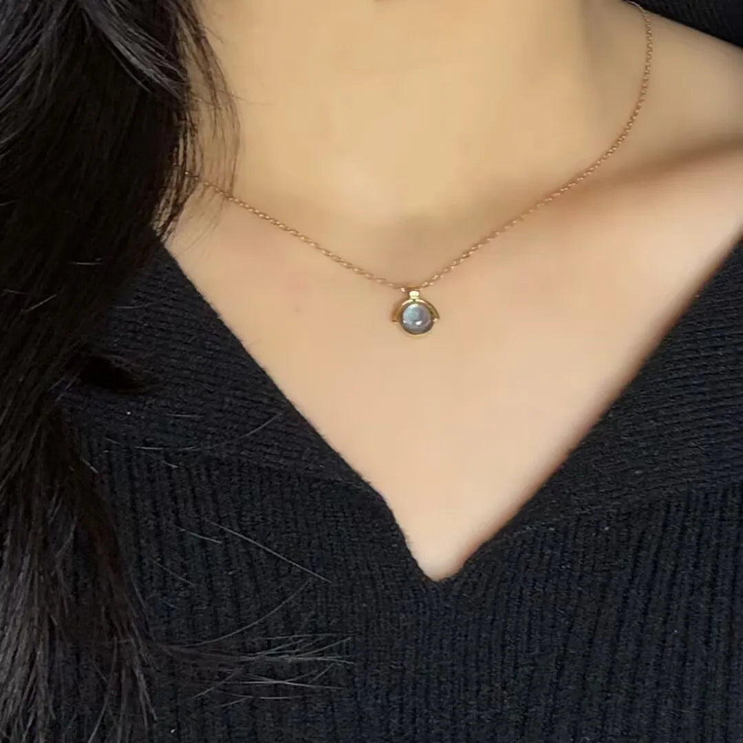 Collier en argent 925 avec un pendentif rond en aigue-marine bleutée, porté sur une femme portant un pull noir.