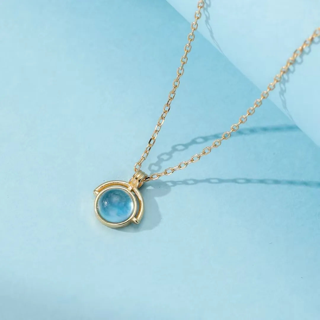 Collier en argent 925 avec une pierre d'aigue-marine ronde et bleue, monté sur une chaîne dorée.