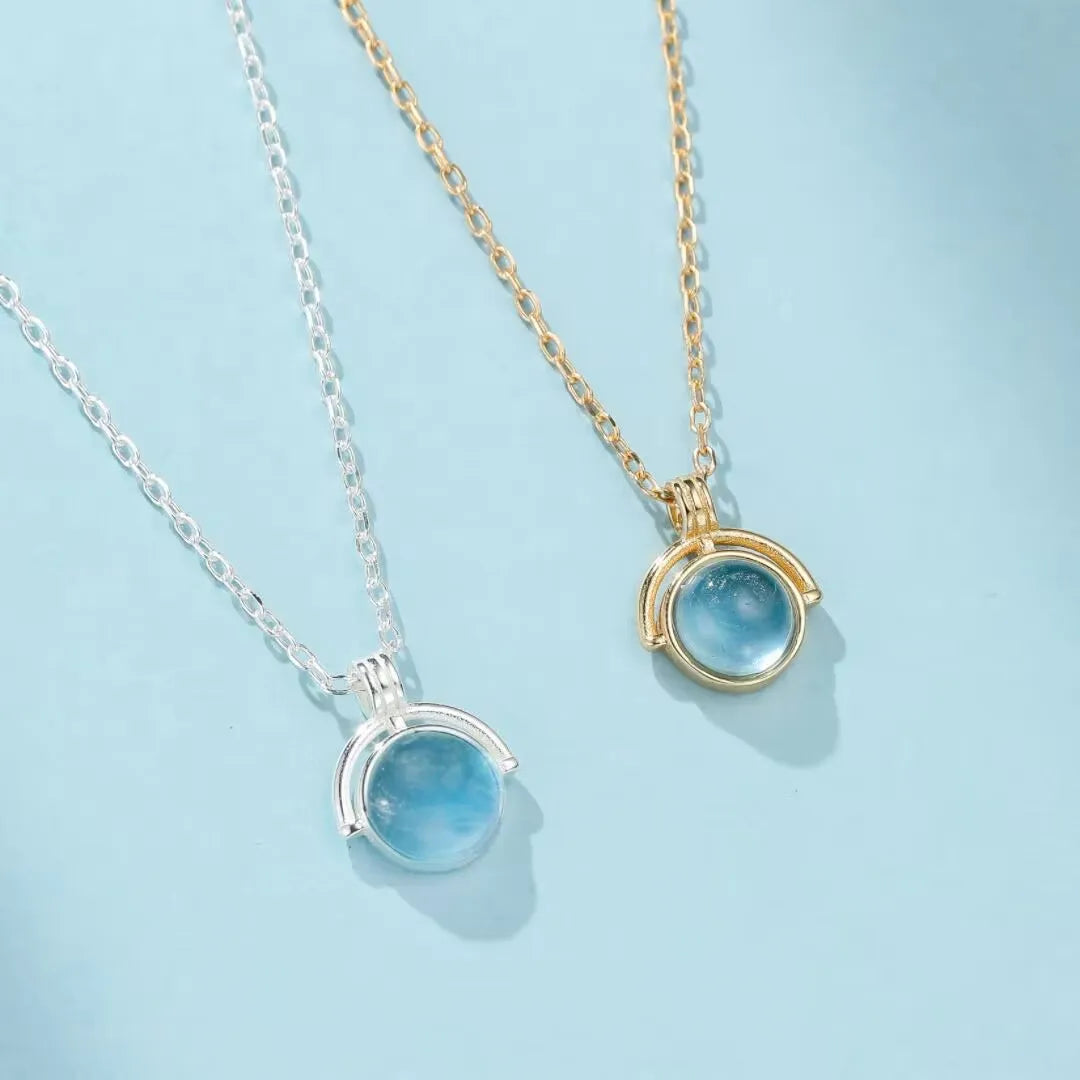 Collier "Mystère d'Océan" en argent avec une pierre d'aigue-marine bleue ronde suspendue à une chaîne dorée ou argentée.