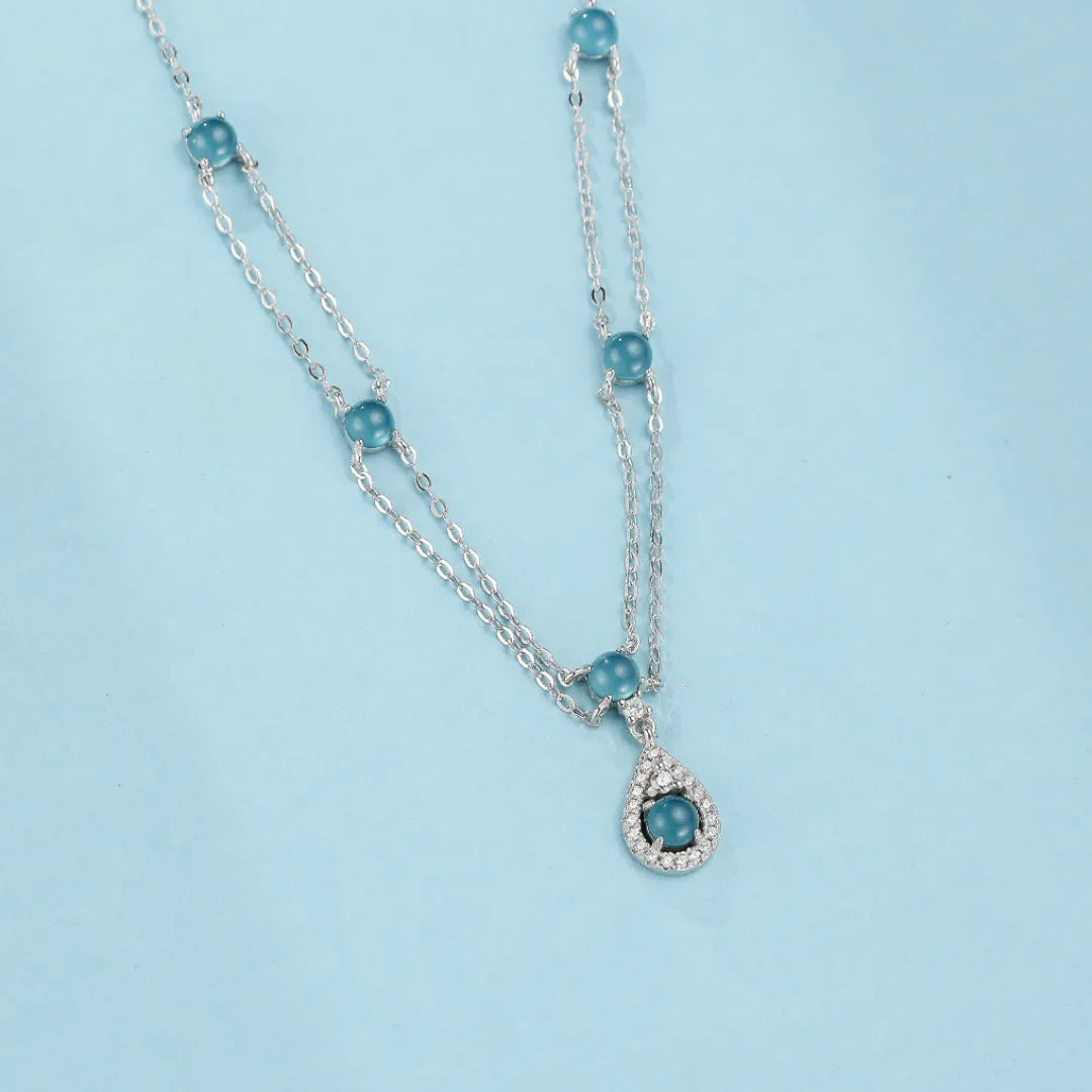 Collier double chaîne en argent orné de perles d'aigue-marine bleues et d'un pendentif en forme de larme serti de zircons scintillants.