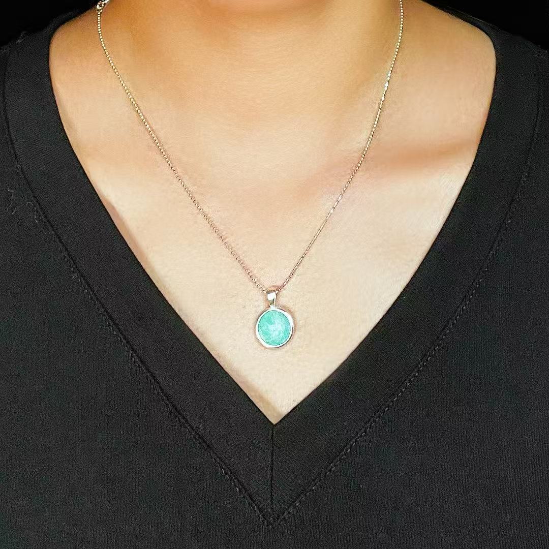 Gros plan sur un collier en argent avec un pendentif rond en amazonite bleu turquoise clair, porté par une femme sur un haut noir.
