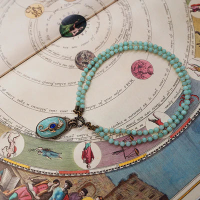 Collier "Voyage Marin" double rangs de pierres d'amazonite et pendentif ovale turquoise avec un saphir bleu au centre, sur un fond de carte astronomique ancienne.