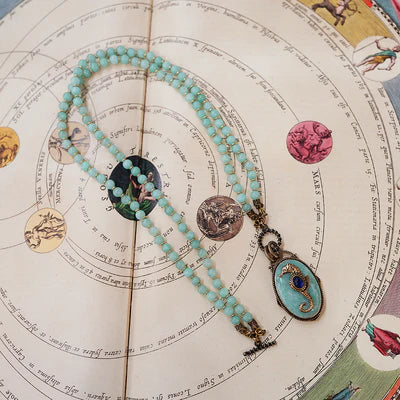 Collier Amazonite "Voyage Marin" avec un pendentif hippocampe bleu et une pierre d'amazonite sur un fond de carte céleste ancienne.