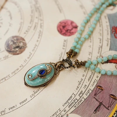 Collier "Voyage Marin" avec pendentif ovale en amazonite orné d'un hippocampe doré et d'une pierre bleue, monté sur une double chaîne de perles bleu-vert clair.