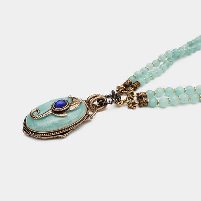 Collier "Voyage Marin" en amazonite, composé d'une pierre centrale ovale bleu pâle ornée d'un cabochon bleu marine, et de deux rangs de perles d'amazonite bleues claires, avec des détails dorés et argentés.