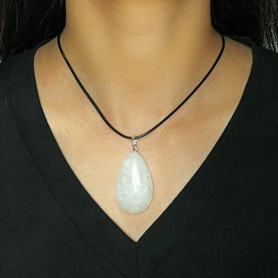 Gros plan sur un collier avec un pendentif en forme de larme en cristal de roche blanc, monté sur un cordon noir, porté par une femme.