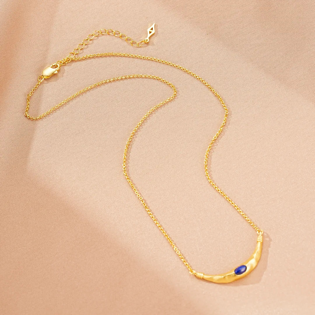 Collier "Allure Mystique" en argent doré or, orné d'un pendentif incurvé martelé et d'une pierre de lapis-lazuli bleue au centre.