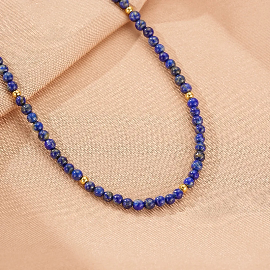Collier "Beauté Astrale" en lapis lazuli avec de petites perles dorées, sur un fond rose poudré.