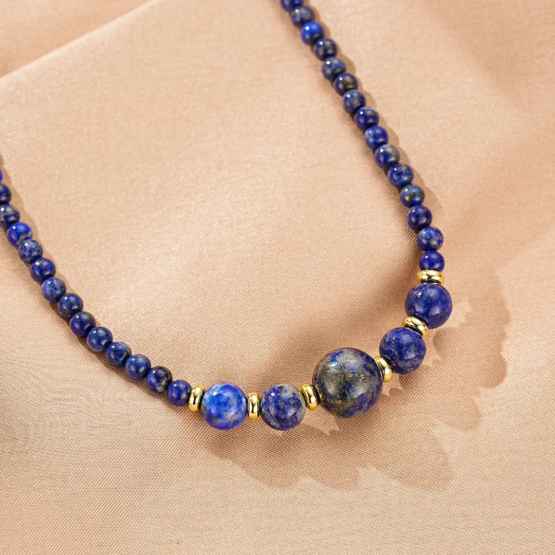 Collier "Équilibre Doux" fait de perles de Lapis Lazuli de différentes tailles et de perles dorées, posé sur un fond beige doux.