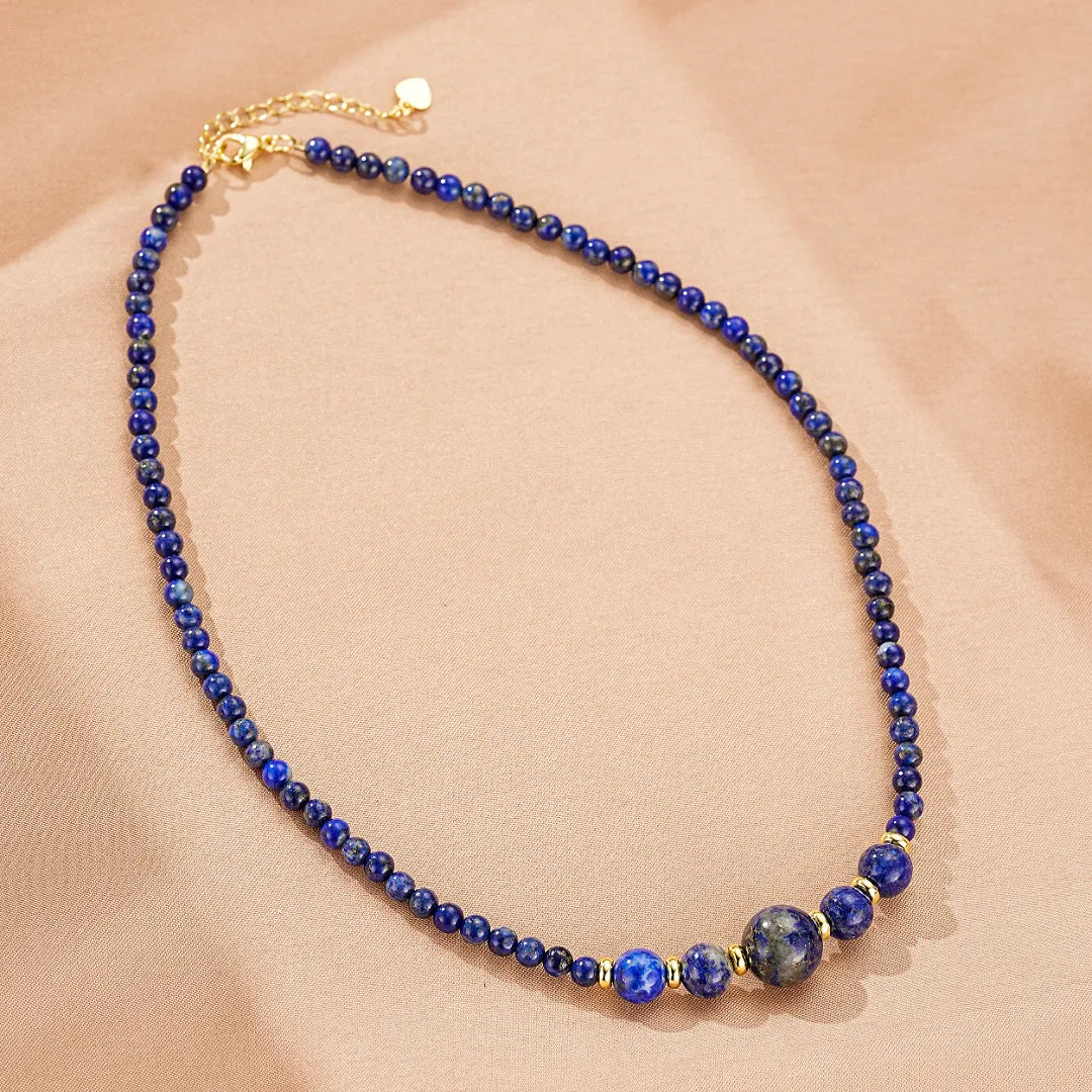 Collier ras du cou fait de petites perles rondes en lapis-lazuli bleu foncé et de quelques perles plus grosses, avec des intercalaires dorés discrets.