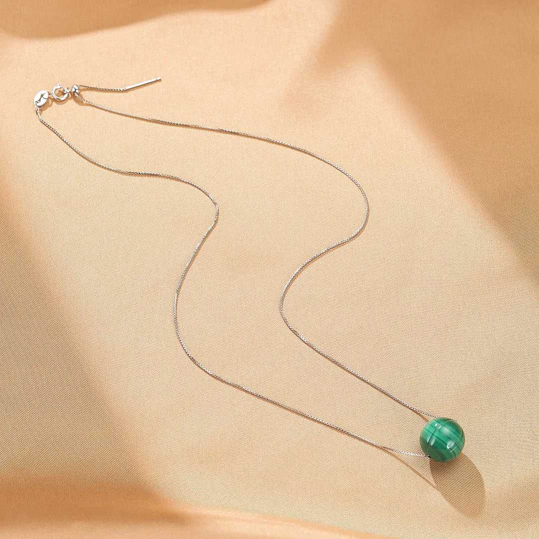 Collier "Beauté Naturelle" en argent avec une unique perle ronde en malachite verte, sur fond beige satiné.