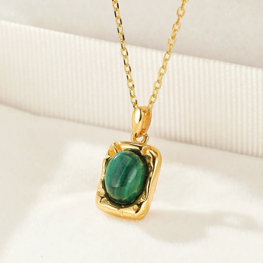 Gros plan sur un collier en argent avec un pendentif rectangulaire doré serti d'une pierre de malachite verte aux motifs naturels distinctifs.