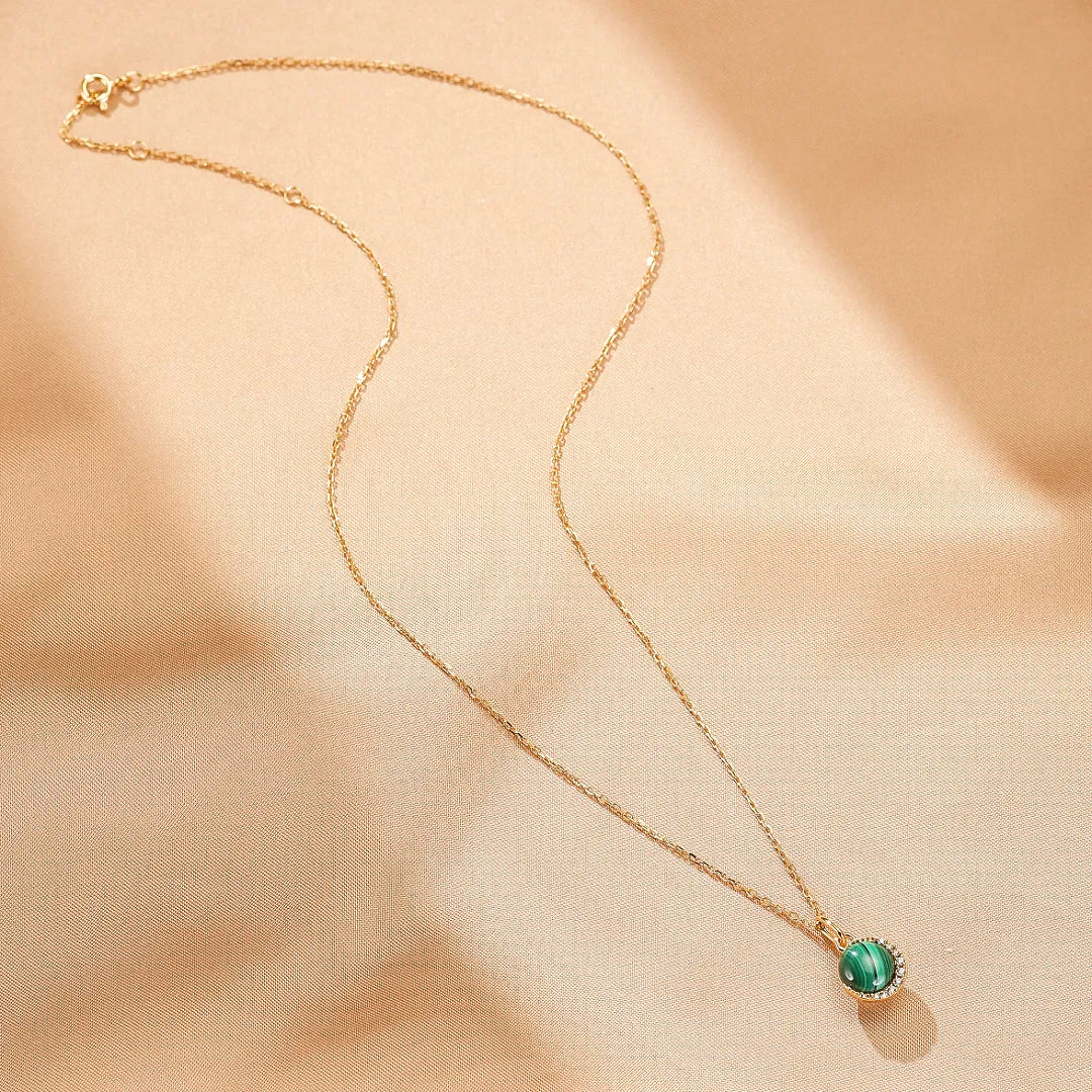 Collier en argent doré avec une pierre de malachite ronde sertie de petits cristaux brillants, sur une chaîne fine.